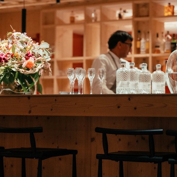 Romantischer Kurzurlaub für Verliebte – Sensoria Dolomites Bar mit Gläsern, Flaschen und Blumenstrauß, Barkeeper im Hintergrund