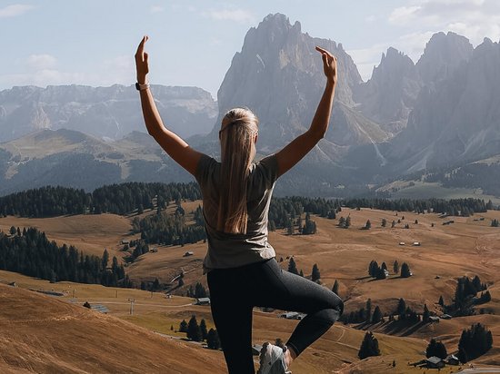 Luxus für die Seele: Ihr Yogahotel in Südtirol Frau macht Yoga im Gebirge mit Blick auf Tal und Berge bei klarem Himmel
