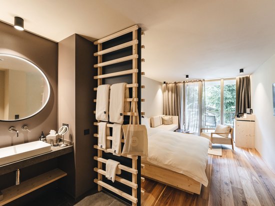 Momente, die bleiben. Im Luxushotel auf der Seiser Alm. Modernes Hotelzimmer mit Holzfußboden, Bett, Sofa und beleuchtetem Badezimmer