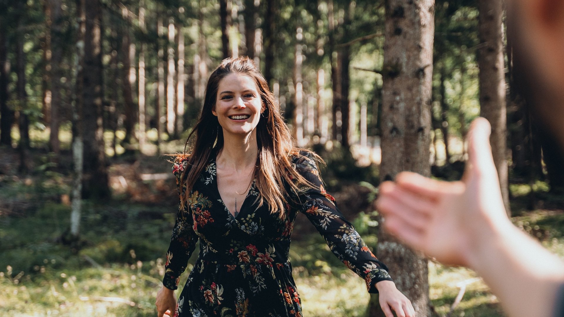 Sensoria Dolomites – Urlaub in Seis am Schlern Frau im blumigen Kleid läuft glücklich auf ausgestreckte Hand im Wald zu