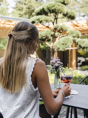 Luxus für die Seele im Kurzurlaub in Südtirol Frau sitzt draußen mit weißem Kleid und hält ein Glas Getränk am Tisch