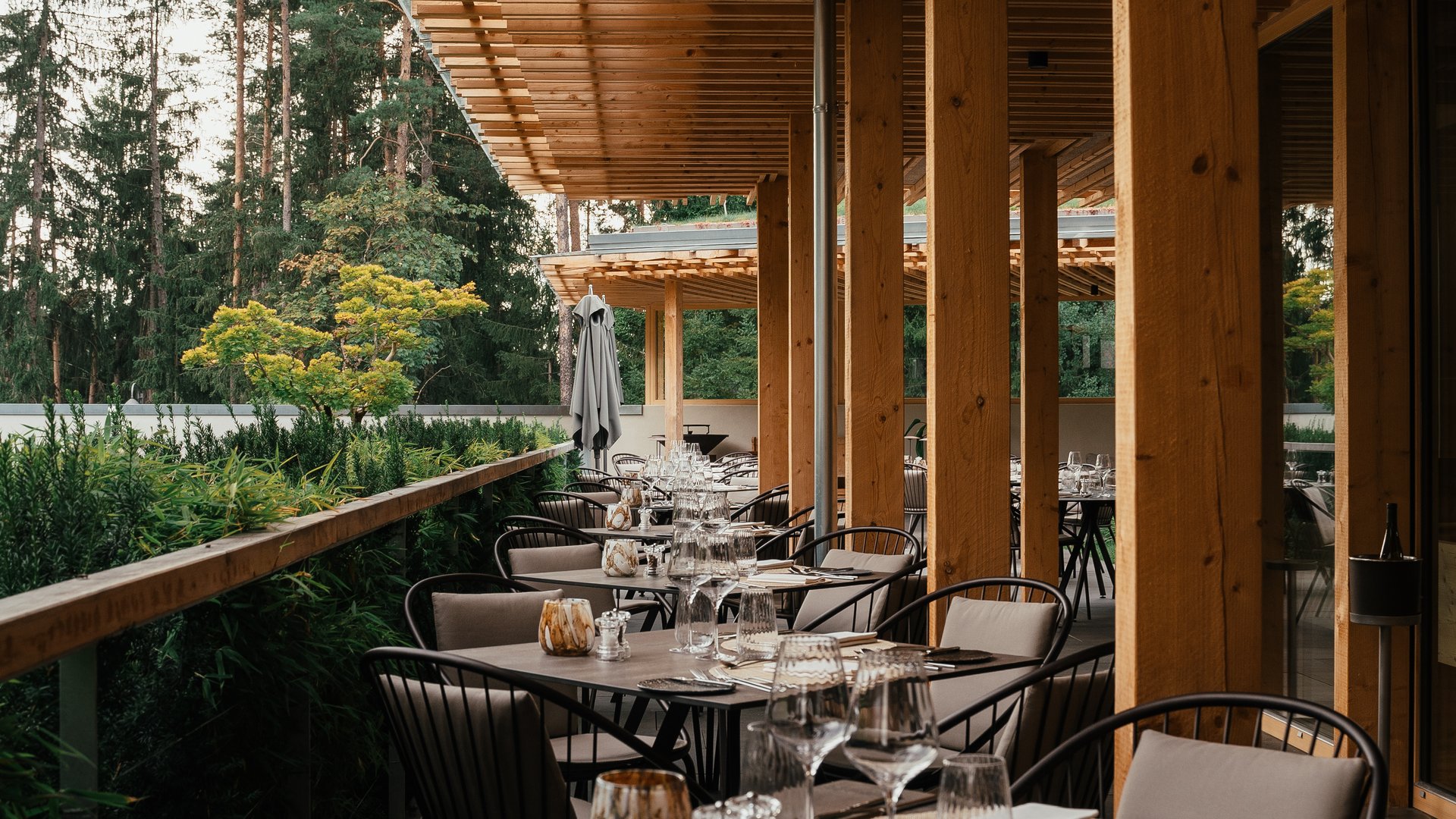 Genussurlaub in Südtirol – Sensoria Dolomites Elegante Außenterrasse eines Restaurants mit gedeckten Tischen aus Holz und Metall