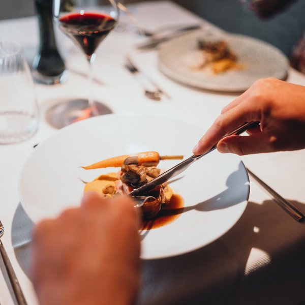 Genussurlaub in Südtirol – Sensoria Dolomites Person schneidet feines Gericht mit Karotte und Pilzen am gedeckten Tisch
