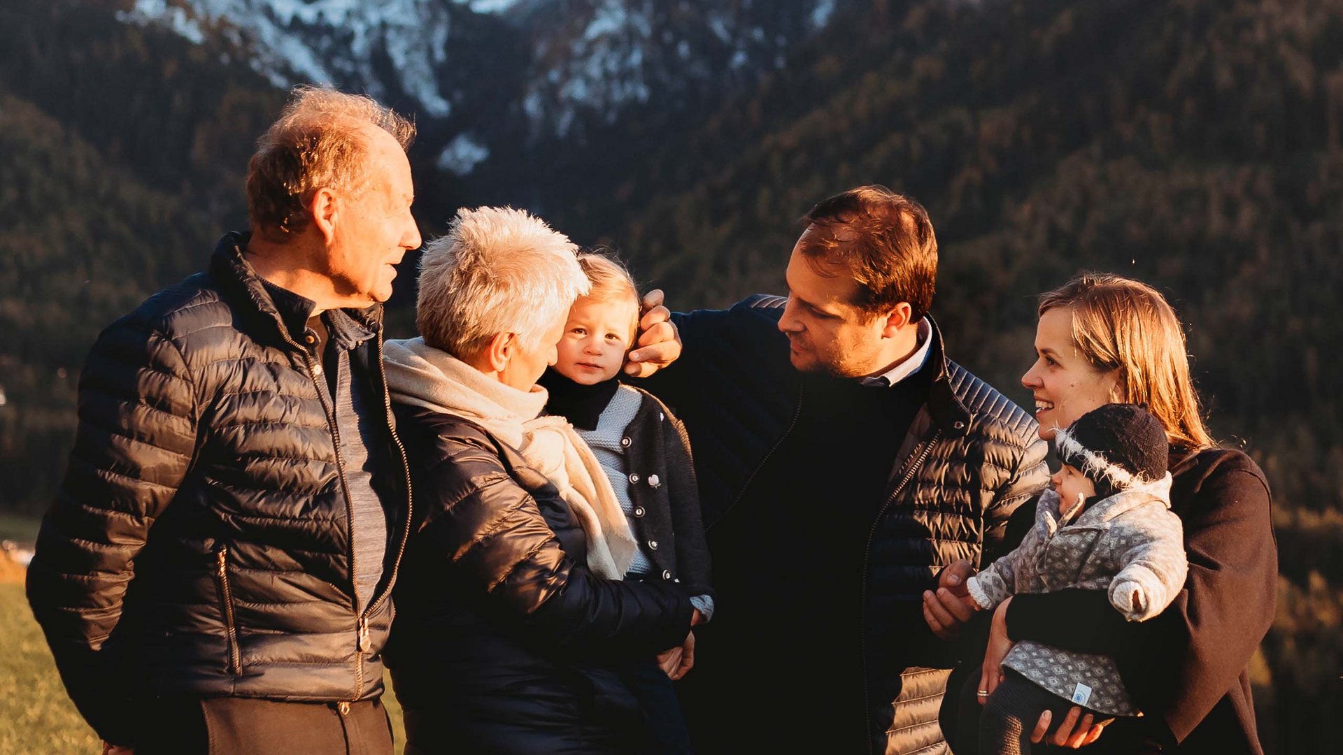 Kraftorte, Lieblingszimmer, Gastgeber mit Herz Mehrgenerationenfamilie in Winterkleidung vor verschneiten Bergen im Freien