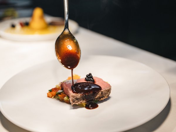 Wellness Aphrodite: Sensoria Dolomites unter den Siegern Sauce wird auf ein Stück rosa gebratenes Fleisch auf einem weißen Teller gegossen