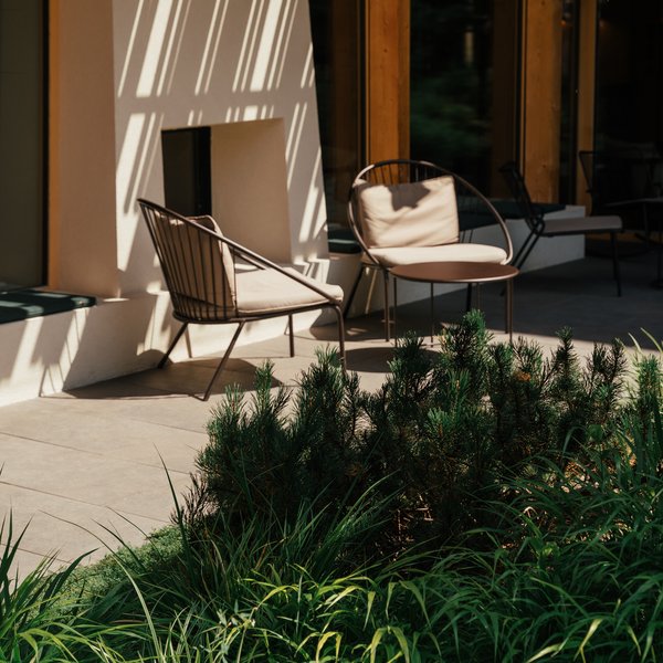 Romantischer Kurzurlaub für Verliebte – Sensoria Dolomites Sonniger Sitzbereich mit Gartenpflanzen und Stühlen vor einem Holzhaus