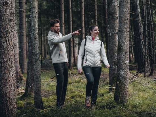 Hotel in Seis am Schlern gesucht? Sensoria Dolomites gefunden! Paar wandert im Wald, Mann zeigt auf etwas, beide tragen Outdoor-Kleidung