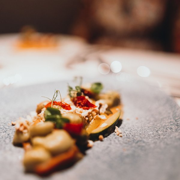 Genussurlaub in Südtirol – Sensoria Dolomites Fein angerichtetes Gourmetgericht auf grauem Teller, unscharfer Hintergrund