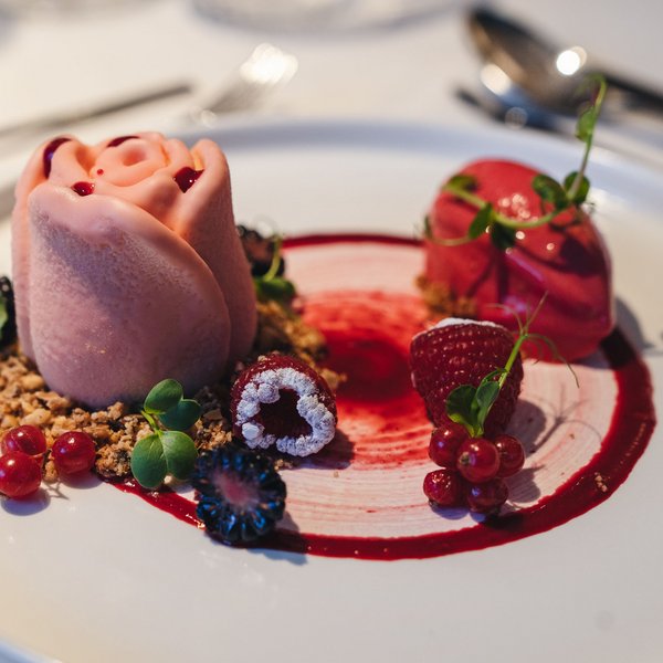 Genussurlaub in Südtirol – Sensoria Dolomites Elegantes Dessert mit Roseförmigem Eis und Beeren auf weißem Teller