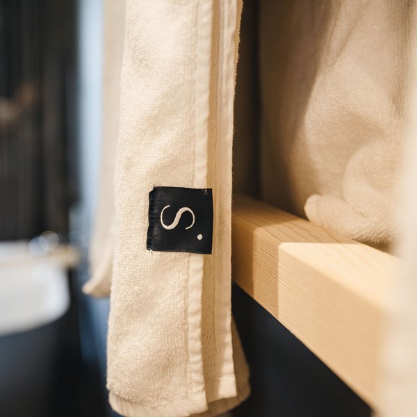 Romantischer Kurzurlaub für Verliebte – Sensoria Dolomites Weißes Handtuch mit schwarzem Etikett an Holzregal im Badezimmer