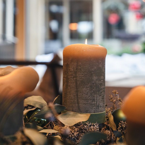 Sensoria Dolomites: Wellnesshotel in den Dolomiten Drei brennende Kerzen auf weihnachtlichem Dekor mit grünem Kranz und Pfauenfeder