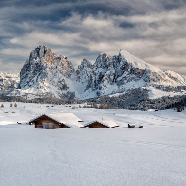 Seiser Alm: Skiurlaub de luxe Verschneite Hütten vor schroffen Bergen unter bewölktem Himmel