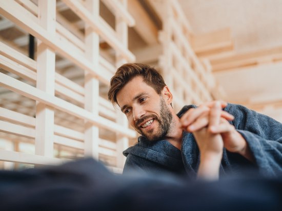 Kostbare Augenblicke in Ihrem Romantikhotel in den Dolomiten Mann im Bademantel lächelt und hält Hände in einem hellen Raum