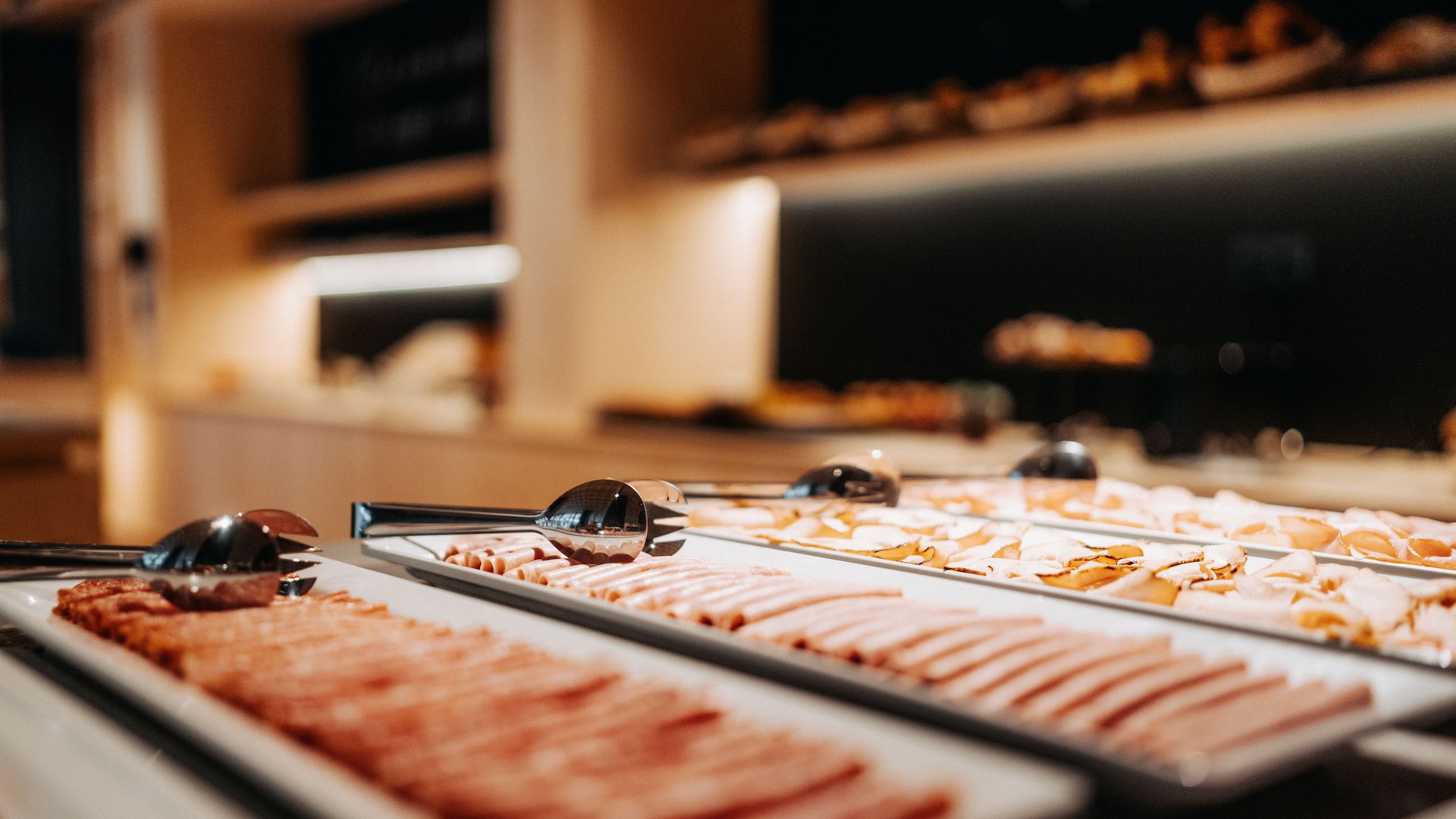 Unser Genussmarkt – perfekt für Ihr Romantikwochenende Buffet mit verschiedenen Aufschnittplatten und Zangen im Fokus