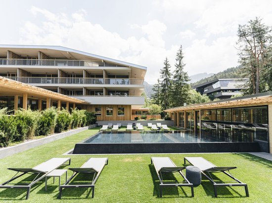 Luxus für die Seele: Ihr Yogahotel in Südtirol Moderner Poolbereich mit Liegestühlen vor einem Hotel und Bäumen im Hintergrund