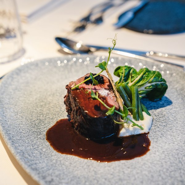 Genussurlaub in Südtirol – Sensoria Dolomites Gourmetgericht mit Fleisch, grünen Bohnen, Blattgemüse und Sauce auf blauem Teller