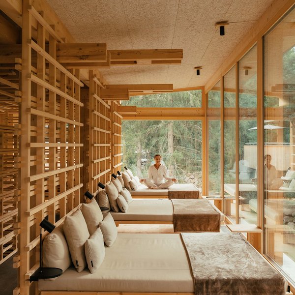 Romantischer Kurzurlaub für Verliebte – Sensoria Dolomites Person meditiert in modernem Holzraum mit Liegen und großer Fensterfront