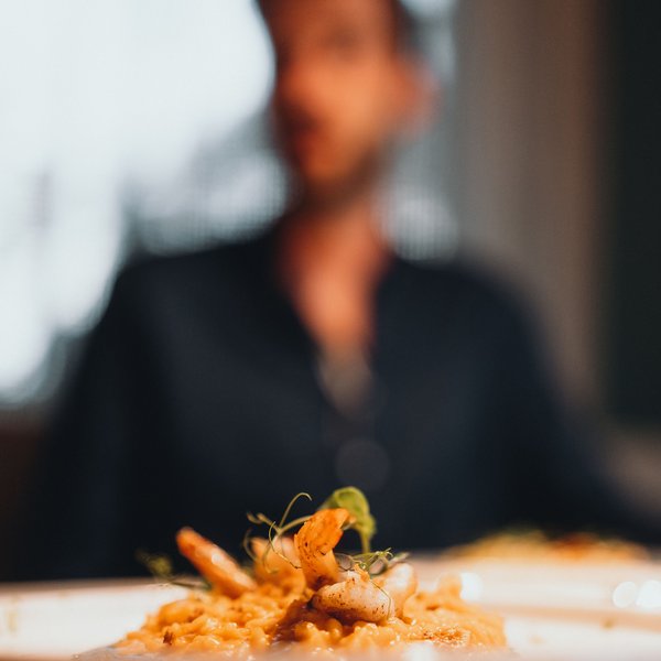 Genussurlaub in Südtirol – Sensoria Dolomites Teller mit Garnelenrisotto vor unscharfer Person im Hintergrund