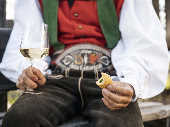 Die Dolomiten – Skiurlaub und so viel mehr Person in traditioneller Tracht hält Weißweinglas und gefülltes Teigstück
