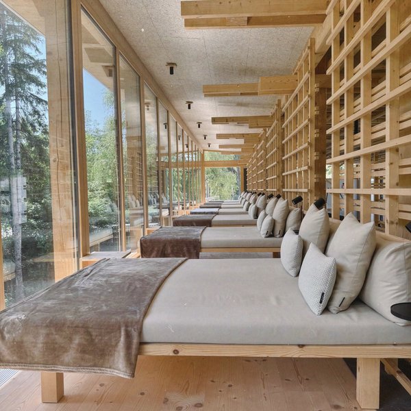 Von Wanderungen auf der Seiser Alm in die Spa Area Reihe von Liegen mit Kissen in einem modernen Holzraum mit großen Fenstern