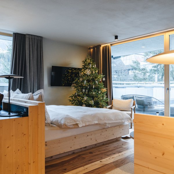 Sensoria Dolomites: Wellnesshotel in den Dolomiten Gemütliches Hotelzimmer mit Weihnachtsbaum und großer Fensterfront mit Bergblick