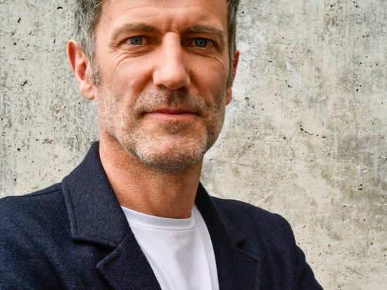 My Olympic Mindset Retreat 2026 Mann mit grauen Haaren und schwarzer Jacke vor grauer Betonwand