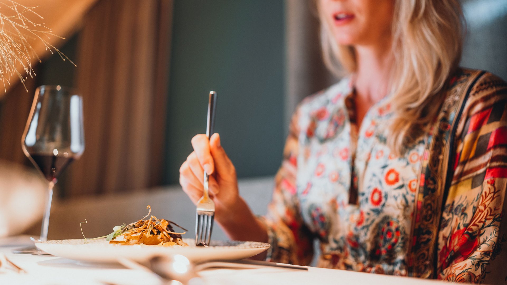 Inclusive services – last-minute South Tyrol holidays Woman dining in elegant restaurant with wine glass and gourmet dish.