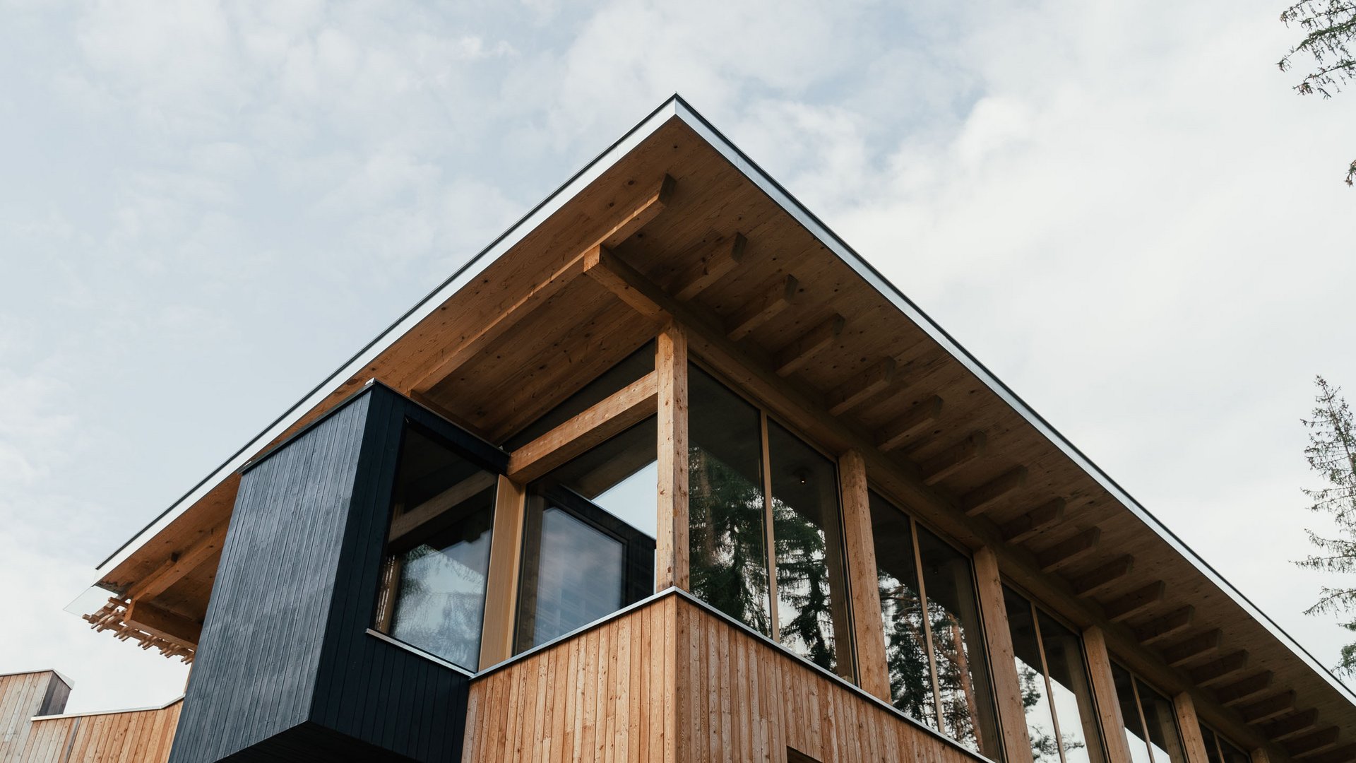 Your hotel in the Dolomites: Sensoria Dolomites Modern wooden house gable with large windows and black protrusion under cloudy sky