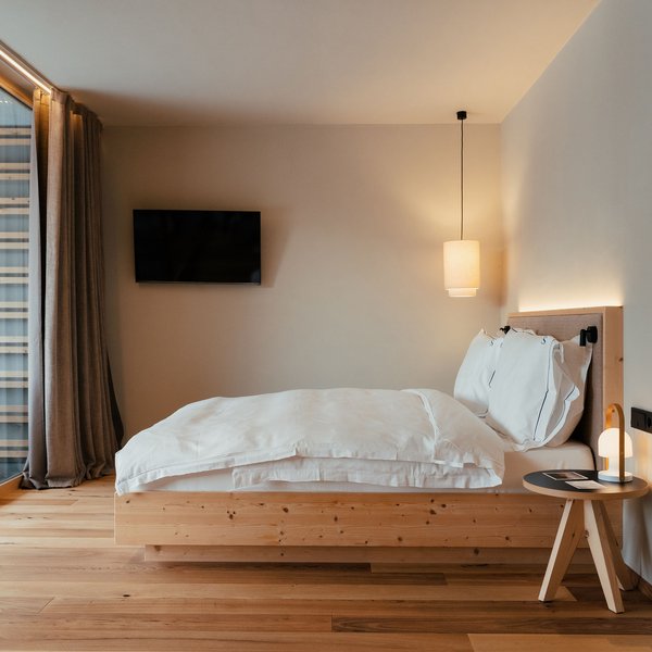 Sensoria Dolomites: Wellnesshotel in den Dolomiten Modernes Schlafzimmer mit Holzdetails, Doppelbett und großem Fenster zur Terrasse