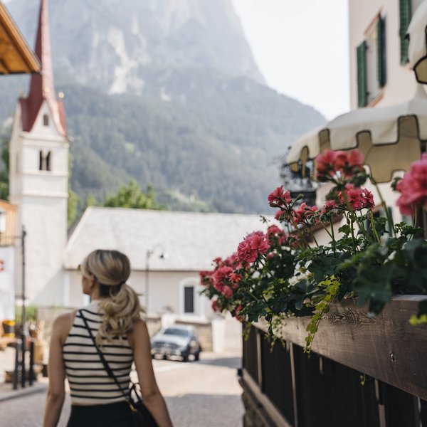 Your hotel in the Dolomites: Sensoria Dolomites Woman walking in mountain village with flowers and church in background
