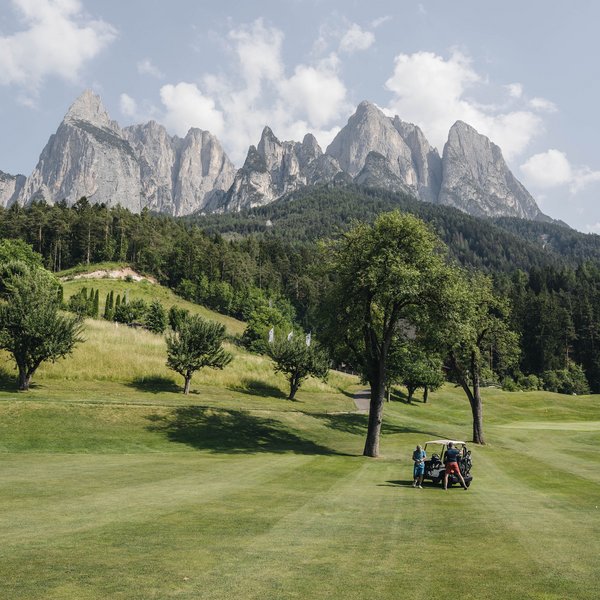 Your hotel in the Dolomites: Sensoria Dolomites Golf players on green fairway with Dolomites mountain range in background
