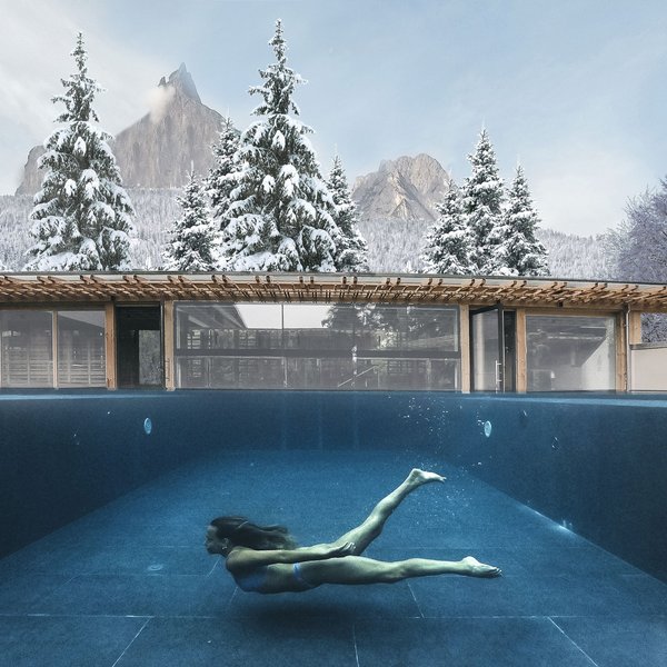 Sensoria Dolomites: Wellnesshotel in den Dolomiten Frau schwimmt unter Wasser im Pool mit schneebedeckten Bäumen und Bergen im Hintergrund