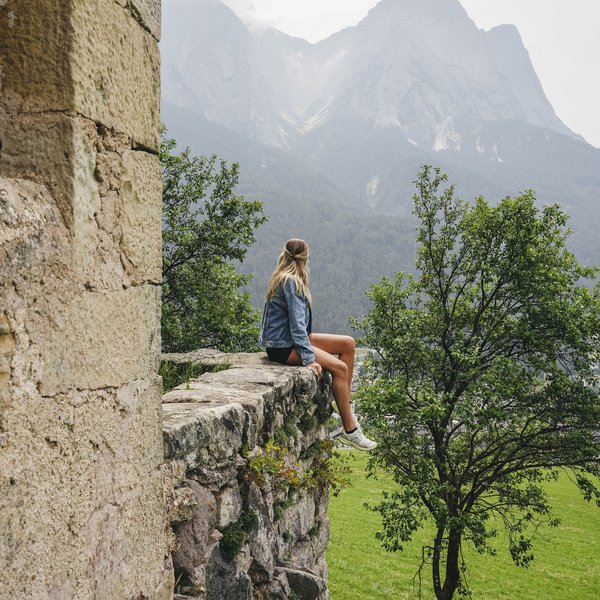 Your hotel in the Dolomites: Sensoria Dolomites Woman sitting on old stone wall overlooking mountains and green landscape