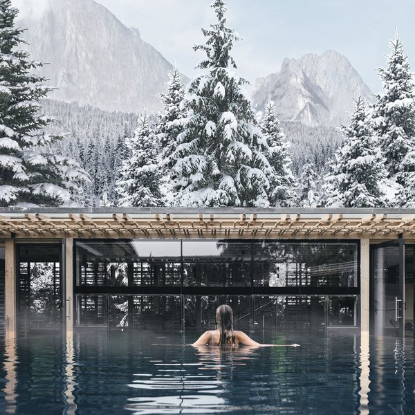 Sensoria Dolomites: Wellnesshotel in den Dolomiten Person im Pool mit Blick auf schneebedeckte Tannen und Berge