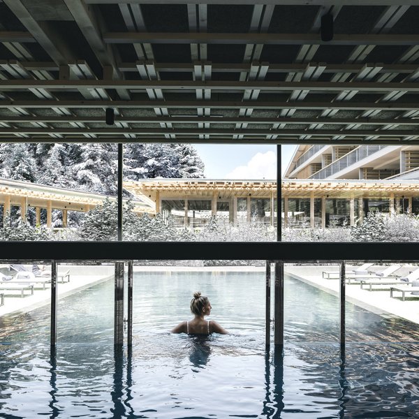 Sensoria Dolomites: Wellnesshotel in den Dolomiten Frau entspannt im Innenpool mit Blick auf verschneite Landschaft und Gebäude