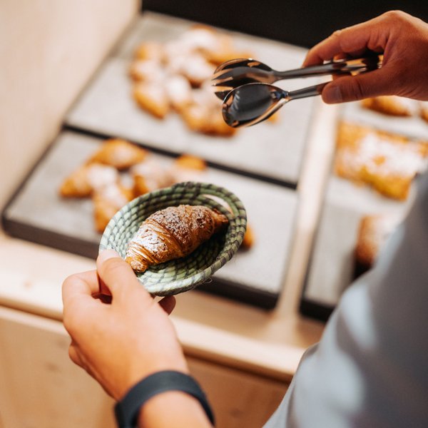 Your hotel in the Dolomites: Sensoria Dolomites Person picking a croissant from a basket with tongs