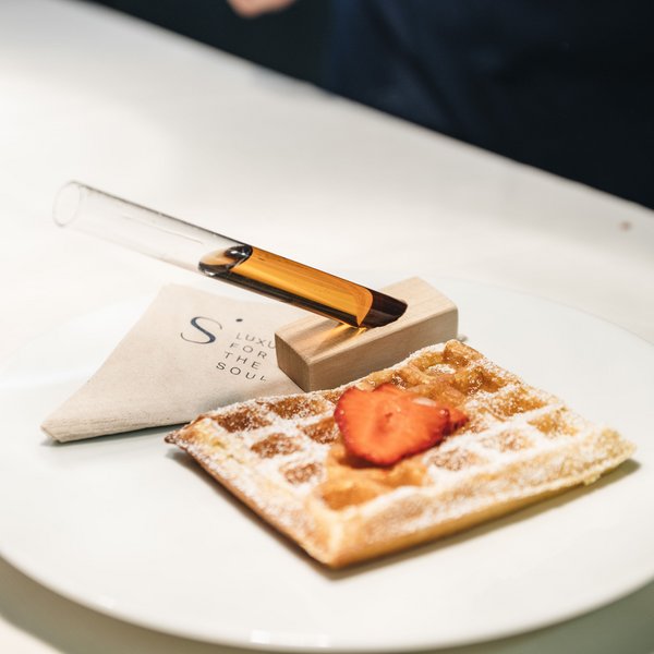 Your hotel in the Dolomites: Sensoria Dolomites Waffle with powdered sugar and strawberry, next to glass tube with syrup