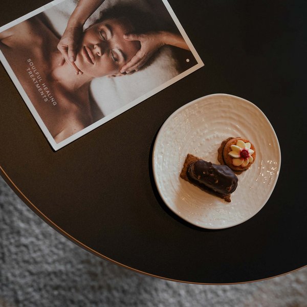 Your hotel in the Dolomites: Sensoria Dolomites Two cookies on a white plate and a wellness brochure on black table