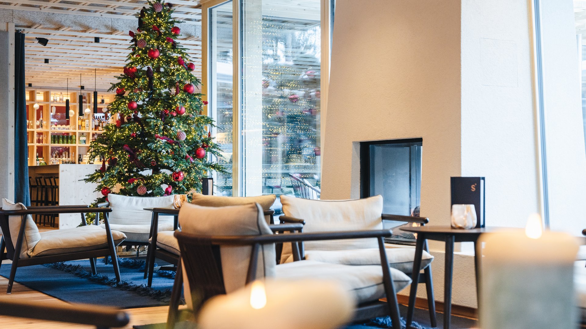 Sensoria Dolomites: Wellnesshotel in den Dolomiten Festlich geschmückter Weihnachtsbaum in einer modernen Lounge mit Sesseln und großen Fenstern