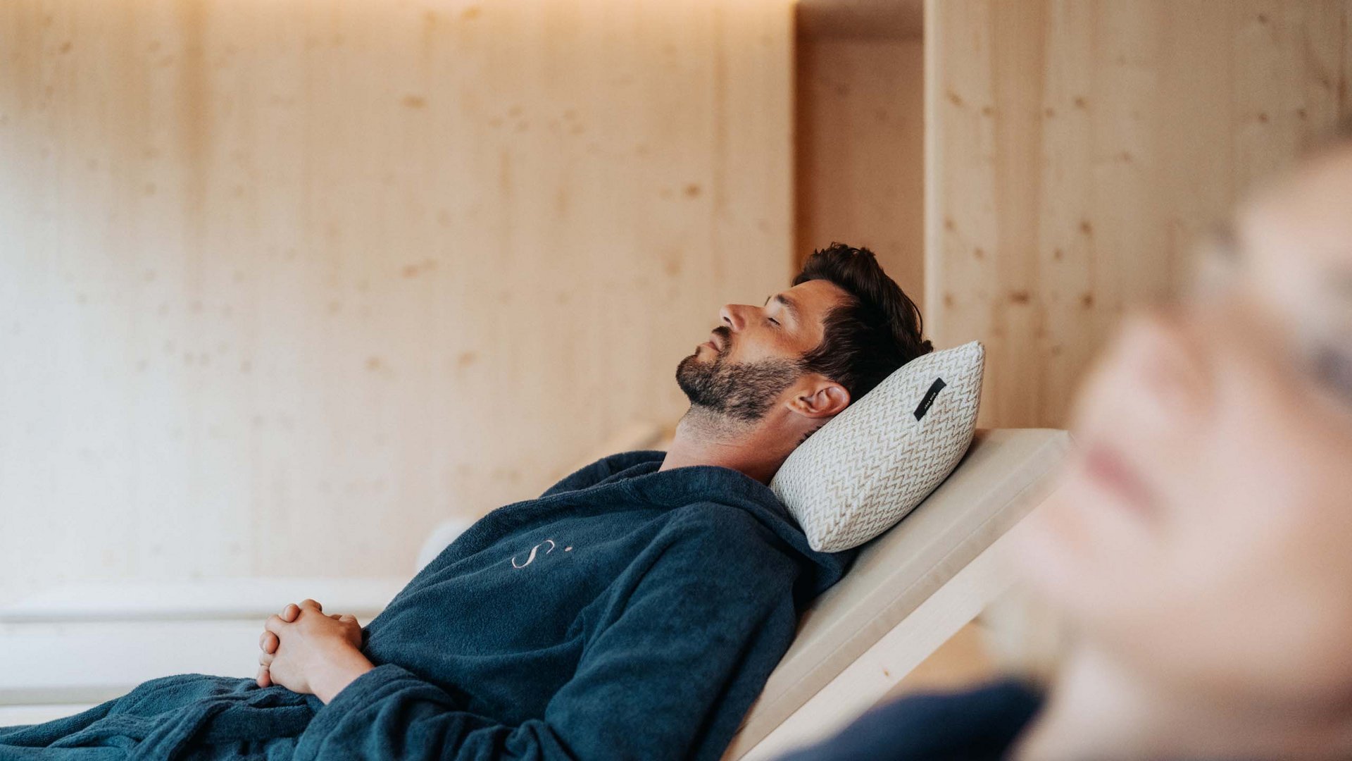 Sensoria Dolomites: Wellnesshotel in den Dolomiten Mann entspannt in Bademantel auf Liegestuhl mit Kopfkissen