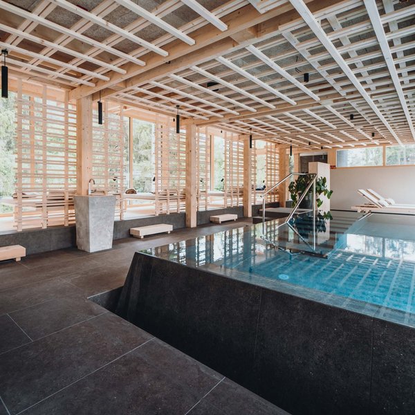 Your hotel in the Dolomites: Sensoria Dolomites Modern indoor pool with wooden ceiling and lounge chairs next to large windows