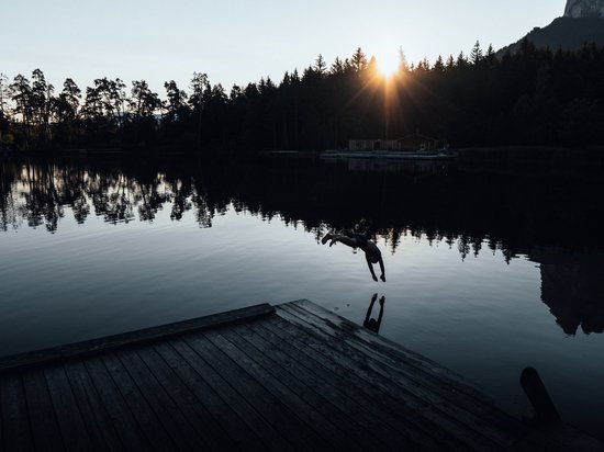 Holidays in the Dolomites – holidays at Sensoria Dolomites Person diving into lake with sunset and trees in the background