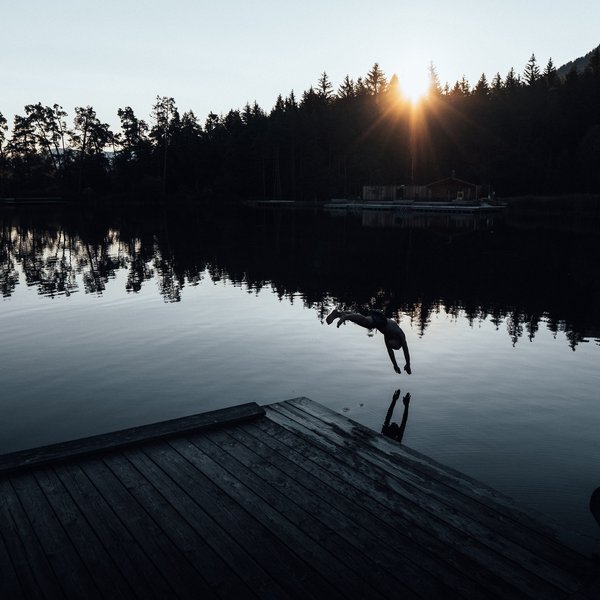 Your hotel in the Dolomites: Sensoria Dolomites Person diving into lake with sunset and trees in the background