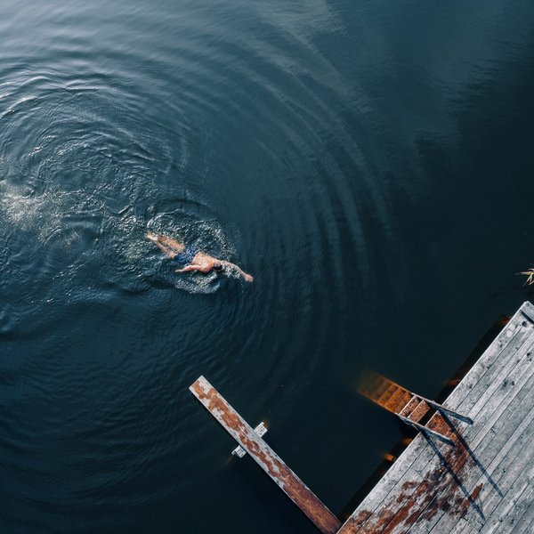 Your hotel in the Dolomites: Sensoria Dolomites Person swimming in dark water near old wooden pier