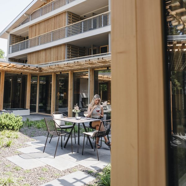 Your hotel in the Dolomites: Sensoria Dolomites Woman sitting outside at table with drinks in front of modern building