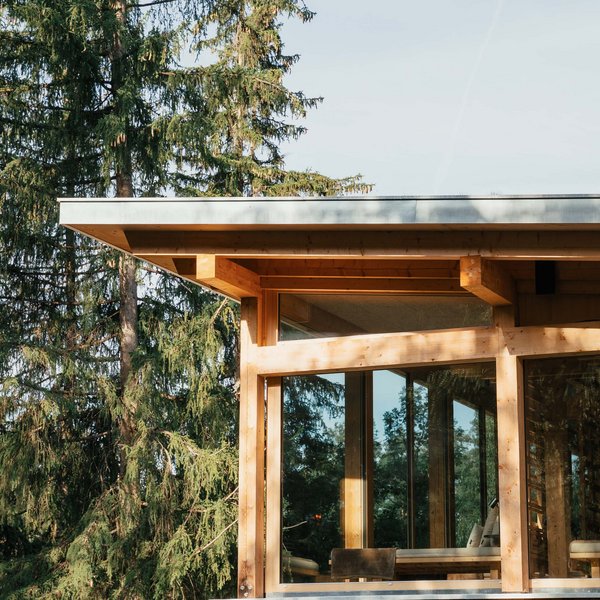 Your hotel in the Dolomites: Sensoria Dolomites Modern wooden house with large windows next to tall pine trees in the forest