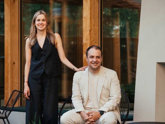 Your hotel in the Dolomites: Sensoria Dolomites Woman standing next to seated man in front of modern wooden house
