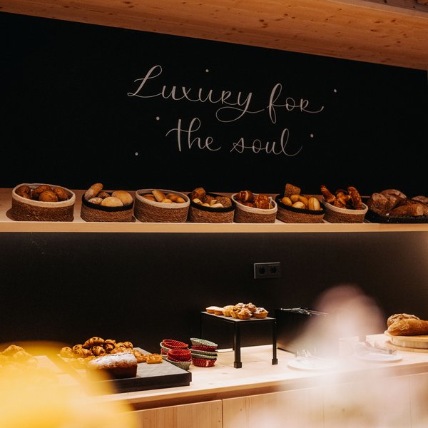 Your hotel in the Dolomites: Sensoria Dolomites Various breads in baskets against black wall with Luxury for the soul text