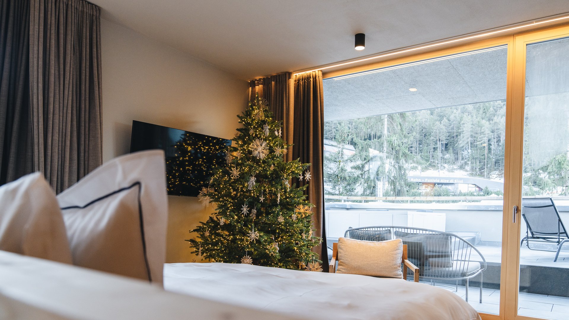 Sensoria Dolomites: Wellnesshotel in den Dolomiten Hotelzimmer mit festlich geschmücktem Weihnachtsbaum und Balkonblick auf eine verschneite Waldlandschaft