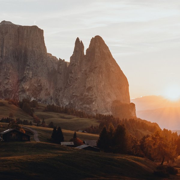 Your hotel in the Dolomites: Sensoria Dolomites Sunset behind rocky peaks in a mountain landscape with cabins